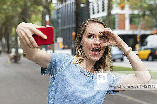 Cheerful businesswoman taking selfie through mobile phone on road