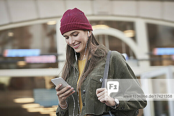 Smiling young woman using mobile phone in front of building