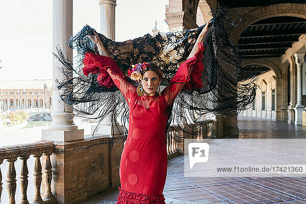 Female flamenco artist holding shawl with hands raised at Plaza De Espana walkway in Seville  Spain