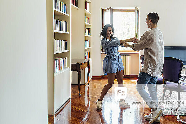 Lesbian women holding hands while dancing in living room at home