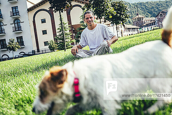 Mid adult man looking at dog while sitting on grass