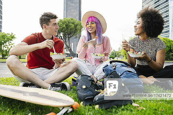 Happy young friends eating salad while sitting at park
