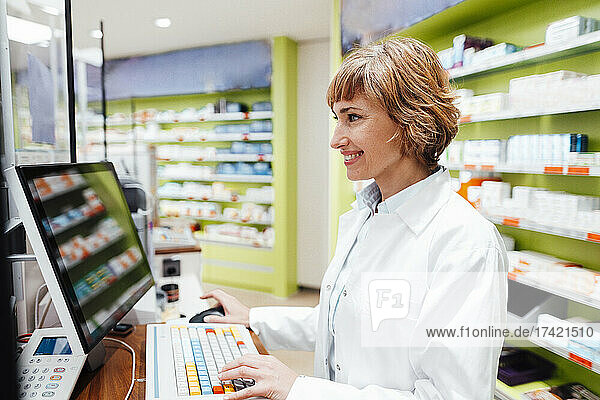 Smiling female pharmacist using computer while standing at medical store