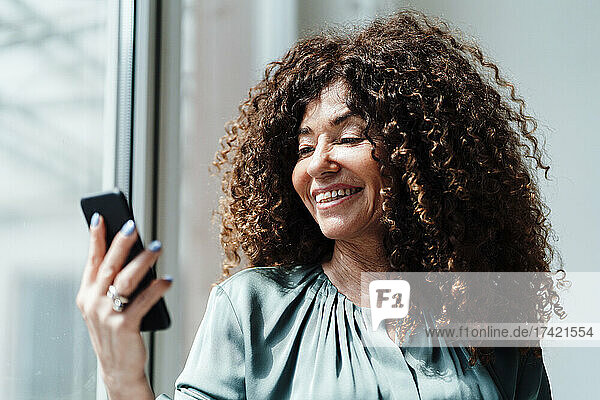 Businesswoman with curly hair using smart phone in office