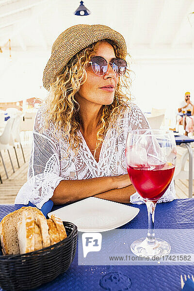 Woman wearing sunglasses sitting with food and drink at table in restaurant