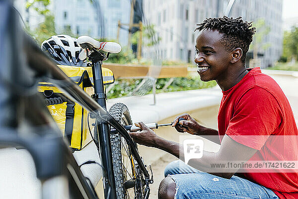 Glücklicher junger Liefermann  der Fahrrad aufpumpt