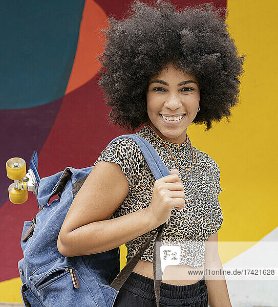 Smiling woman wearing Leopard print top while carrying backpack with skateboard