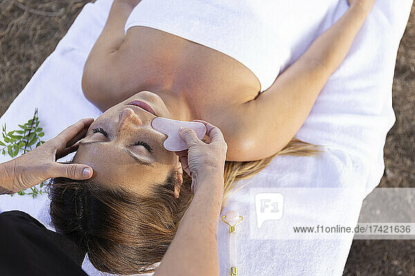 Masseuse giving facial massage to customer lying on table