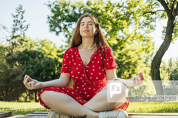 Woman practicing yoga while sitting cross-legged at park