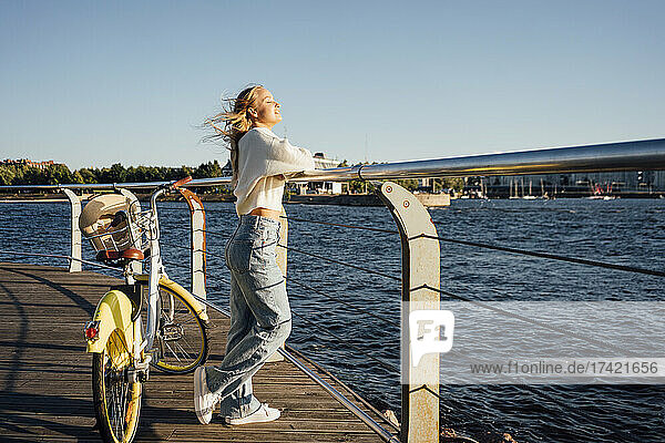 Woman with bicycle standing by railing at boardwalk