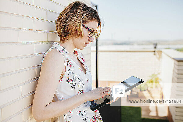 Businesswoman using digital tablet while leaning on wall