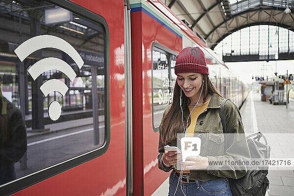 Smiling woman using mobile phone by train at railroad station