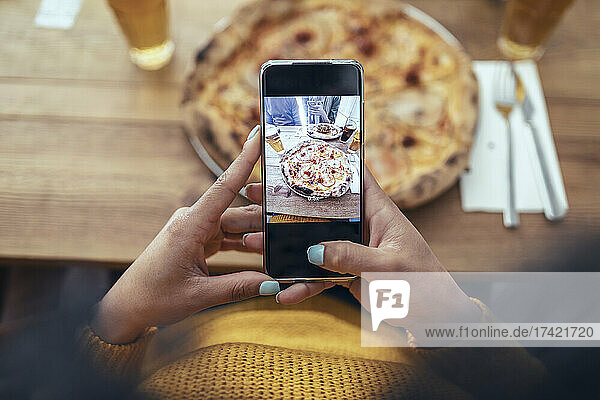 Young woman photographing pizza through smart phone