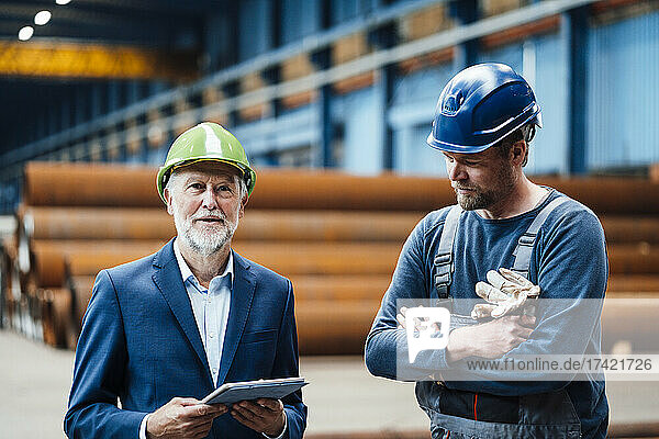 Male manager with digital tablet standing by warehouse worker in factory
