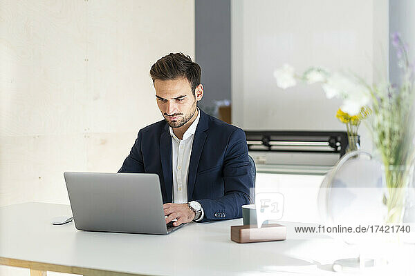 Young businessman using laptop while sitting at desk in office