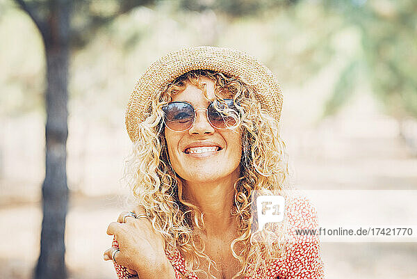 Smiling mature woman with curly blond hair wearing sunglasses and hat