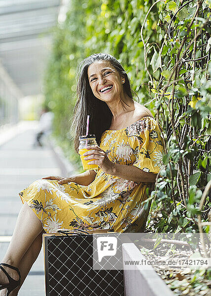 Happy woman having juice while sitting in front of plants