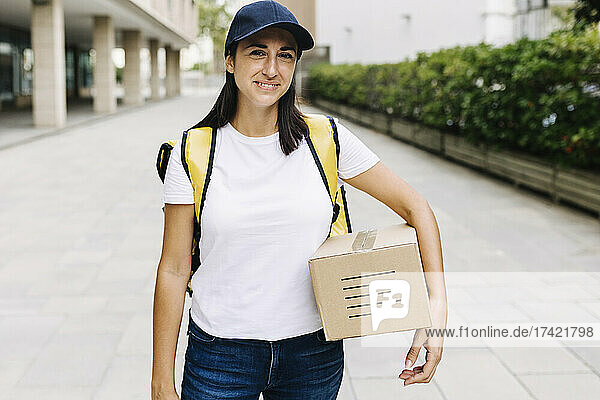 Delivery woman with box standing on footpath