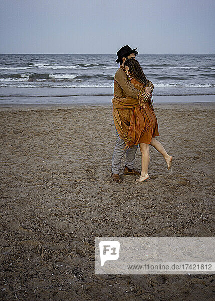 Freund umarmt Freundin in Decke gehüllt am Strand