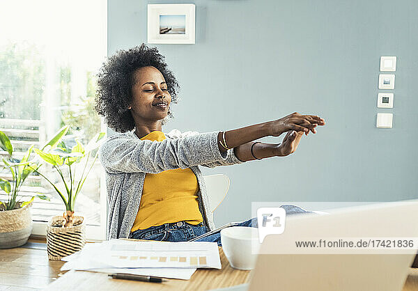 Smiling female freelancer stretching hands at home