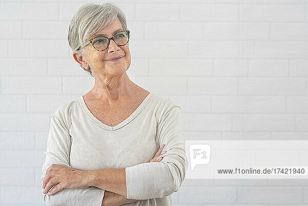 Smiling senior woman contemplating while standing with arms crossed