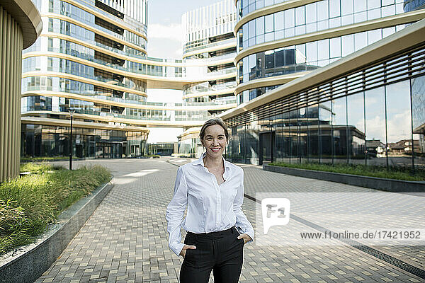 Smiling businesswoman with hands in pockets standing on footpath