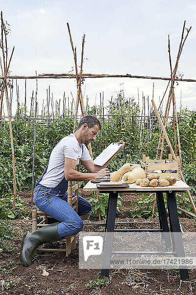 Male farmer with clipboard sitting on chair at agricultural field