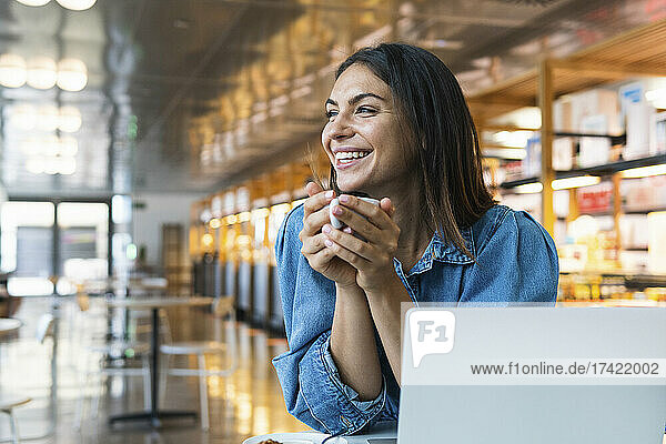 Happy businesswoman with laptop having coffee at cafe