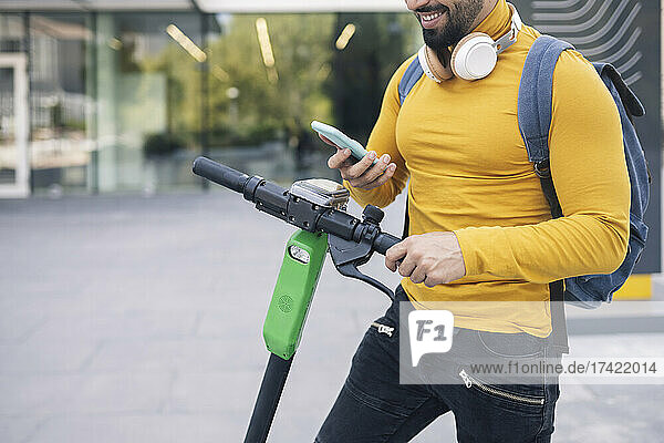 Mann mit Rucksack mietet Elektroroller über Mobiltelefon