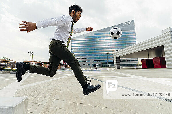 Businessman playing with soccer ball in city