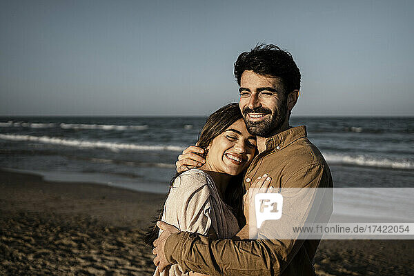 Happy young couple embracing while standing at beach