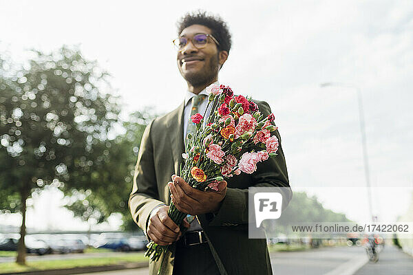 Businessman holding bouquet while standing on road