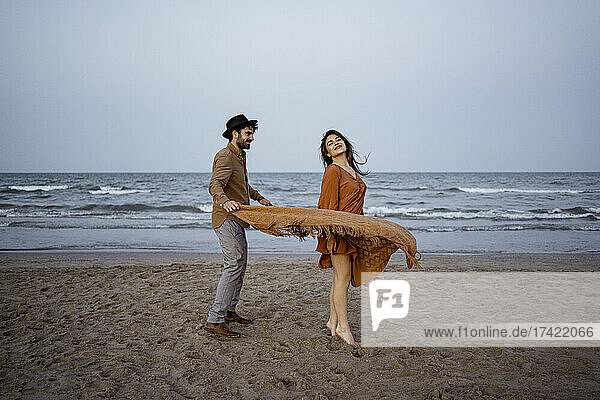 Couple playing with blanket on beach during vacations