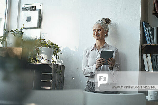 Smiling female freelancer with digital tablet standing at cafe