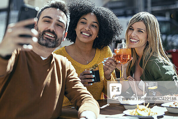 Bärtiger Mann macht Selfie mit Freundinnen  die im Restaurant etwas trinken
