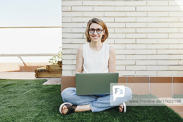 Smiling businesswoman with laptop sitting at terrace