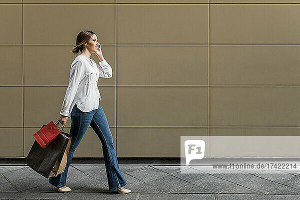 Woman looking away while walking with shopping bags on footpath