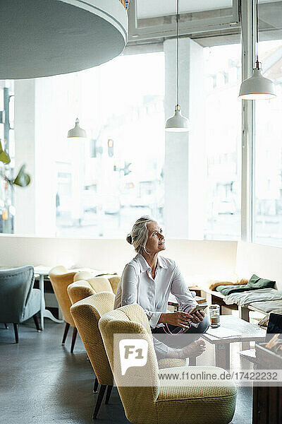 Nachdenkliche Geschäftsfrau sitzt mit gekreuzten Beinen auf einem Stuhl im Café