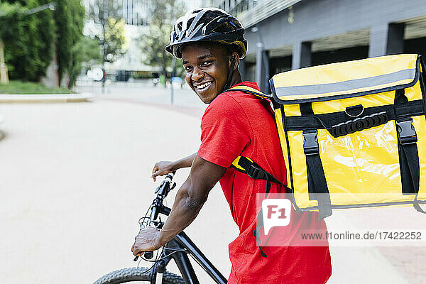 Happy young delivery man wearing backpack sitting on bicycle