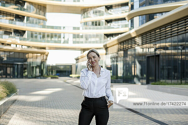 Smiling female professional talking on smart phone outside office building