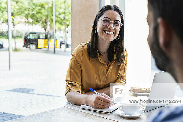 Smiling businesswoman looking at man while working at coffee shop