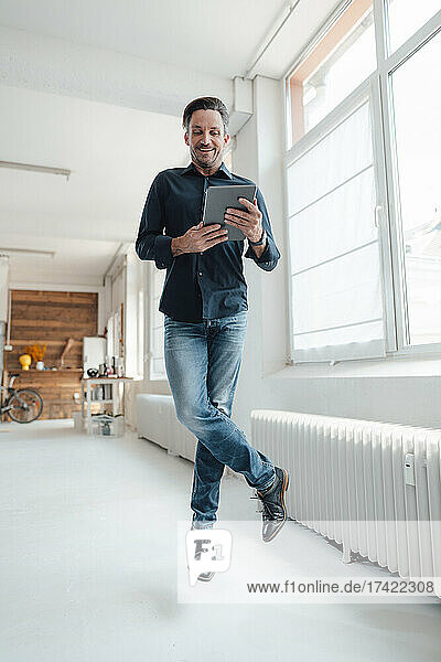 Glücklicher Geschäftsmann nutzt digitales Tablet  während er im Büro springt