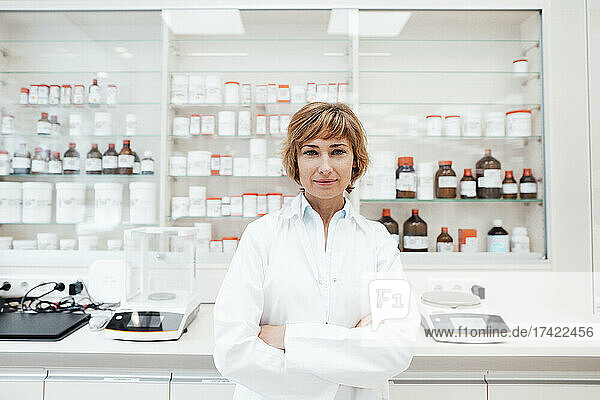 Confident female pharmacist with arms crossed standing at pharmacy