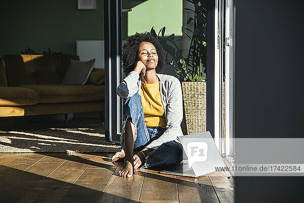 Woman with eyes closed relaxing in sunlight while sitting on floor at home