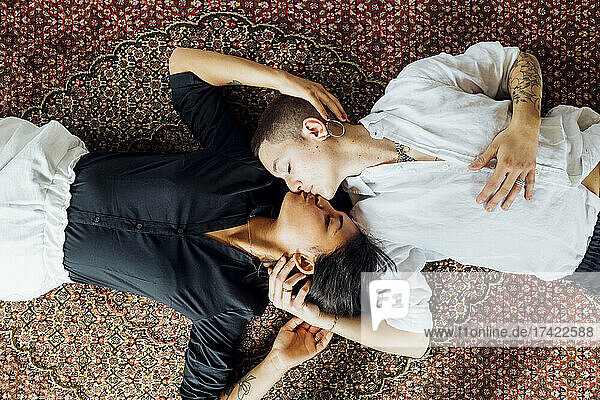 Young multi-ethnic lesbians kissing while lying on carpet at home
