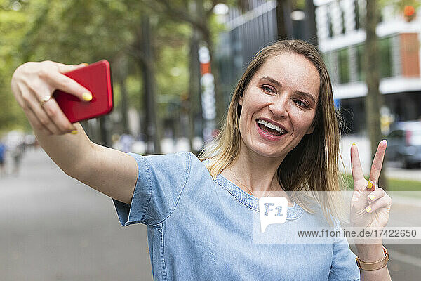 Businesswoman gesturing peace sign while taking selfie through smart phone