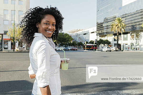 Smiling businesswoman holding drink while standing at city street