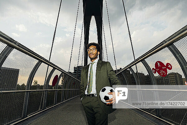 Businessman with soccer ball standing on bridge during sunset