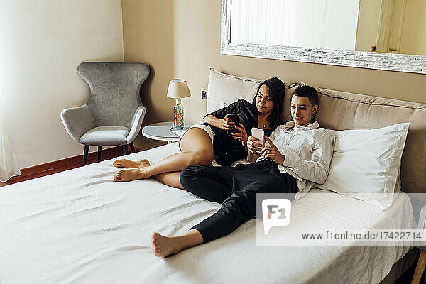 Lesbisches Paar benutzt Mobiltelefone  während es zu Hause im Bett liegt