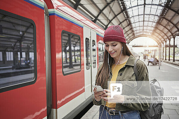 Young female passenger using smart phone while listening music through headphones by train
